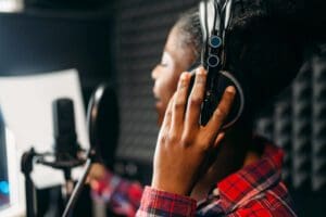 Young woman in headphones songs in audio recording studio. Musician listens composition, professional music mixing